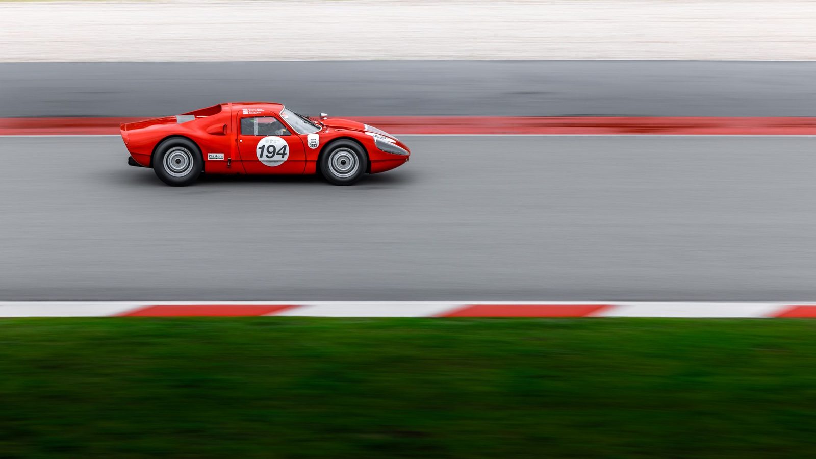 Ein roter Rennwagen mit Startnummer in voller Fahrt auf der Rennstrecke